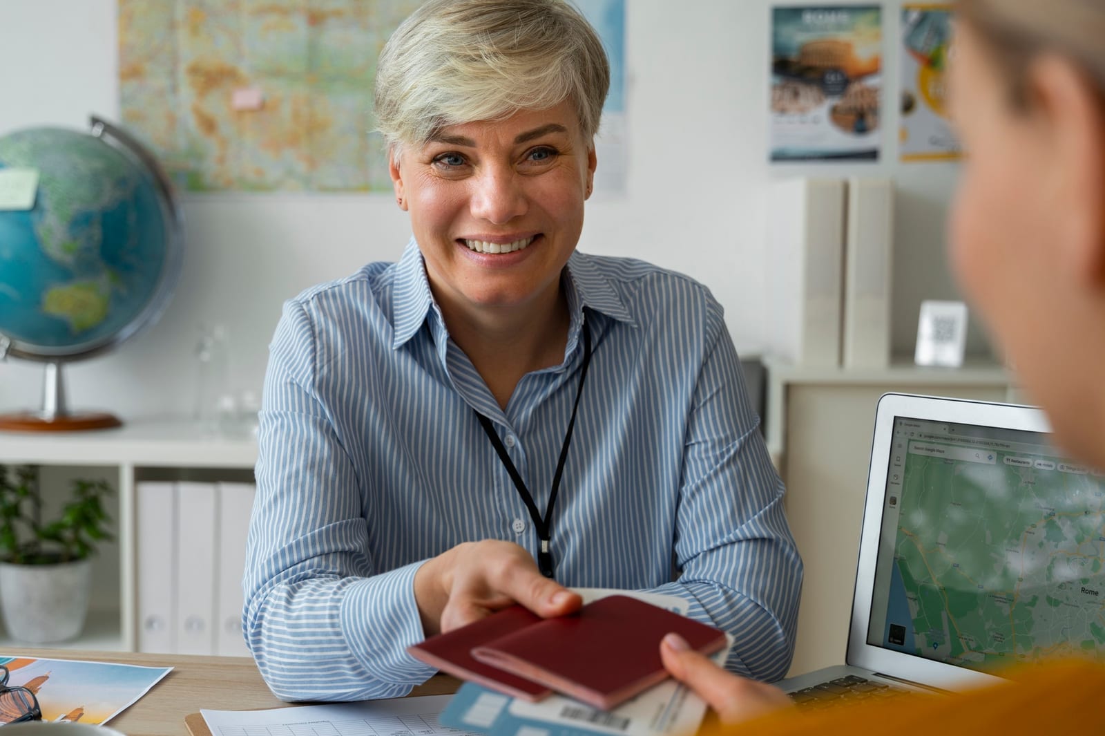 Agente de viagens entrega passaportes a uma cliente, com globo e mapas ao fundo